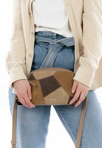 Braune und beige Patchwork-Handtasche mit runder Form, aus Leder gefertigt, mit einem langen, verstellbaren Tragegurt und subtilen Logo-Details.