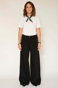 Jean noir à jambes larges et taille haute, associé à un t-shirt blanc uni. Un foulard noir à motifs est noué autour du cou pour accentuer la tenue.