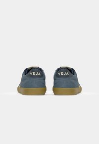 Sneakers bleumarin din suede cu o formă rotundă, accente bej și o talpă din cauciuc. Logo-ul "VEJA" vizibil pe călcâi. Design minimalist.