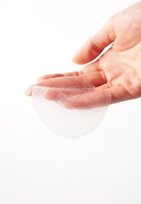 Transparent sirkulært gelpad holdt i en hånd, med en teksturert overflate og en glatt underside, mot en hvit bakgrunn.