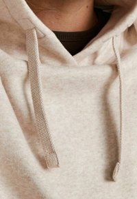 Sudadera de un suave color beige claro, con textura suave, cordones ajustables y una capucha acogedora, adornada con un sutil patrón moteado.