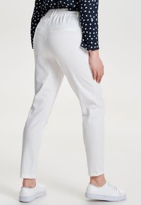 Vita, avsmalnande byxor med elastisk midja och bakfickor, kombinerat med vita sneakers. Tyget verkar vara slätt och lätt.