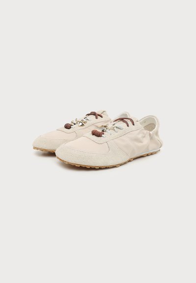 Paire de chaussures décontractées beige clair en daim et tissu mélangés, passants de lacets marron, et semelles en caoutchouc texturées couleur beige sur fond blanc.