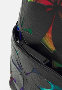 Musta rakenteellinen nahkarepusta, jossa on leikattuja kukkakuormia, paljastaen sisällä kimaltelevia värejä. Vetoketjukiinnitys mustilla metalliosilla.