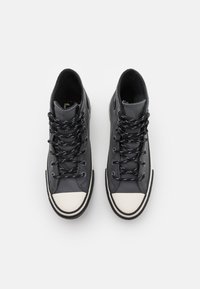 Hoge sneakers van donkergrijs leer met zwart-witte accenten. Voorzien van zwarte veters met witte stippen en een witte rubberen neuskap.