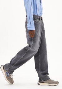 Grijze spijkerbroek met een losse pasvorm, voorzien van een klassiek vijfzakkenontwerp. Gecombineerd met grijze en blauwe sneakers en een lichtblauw gestreefd shirt.