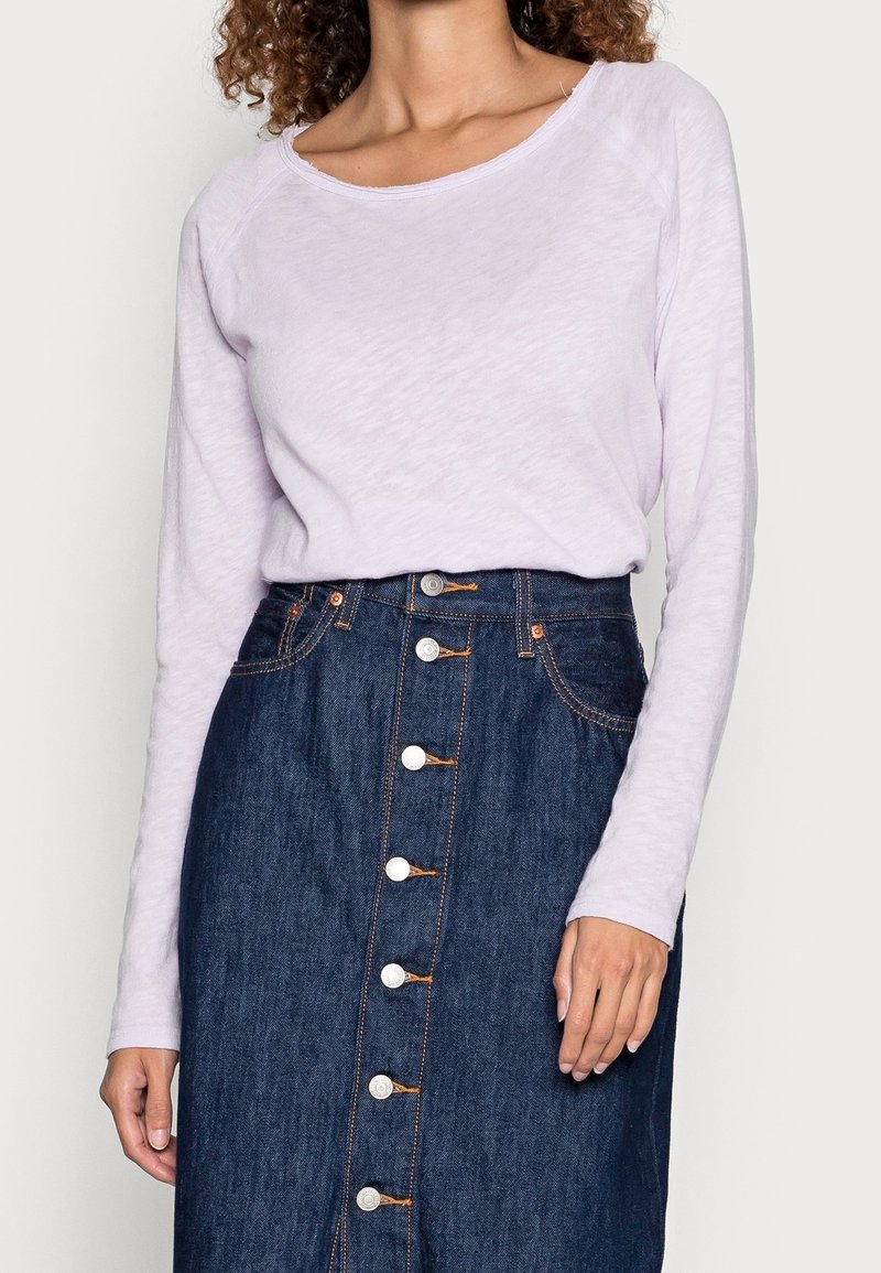 Ljuslila långärmad topp med bred halsringning, kombinerad med en mörk denimkjol med knappframsida och orange sömnadsdetaljer.