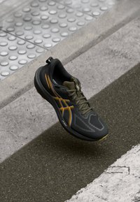 Black athletic shoe with a textured mesh upper, featuring orange and blue accents, a rounded toe, and a cushioned sole for support.