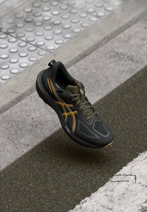 Black athletic shoe with a textured mesh upper, featuring orange and blue accents, a rounded toe, and a cushioned sole for support.