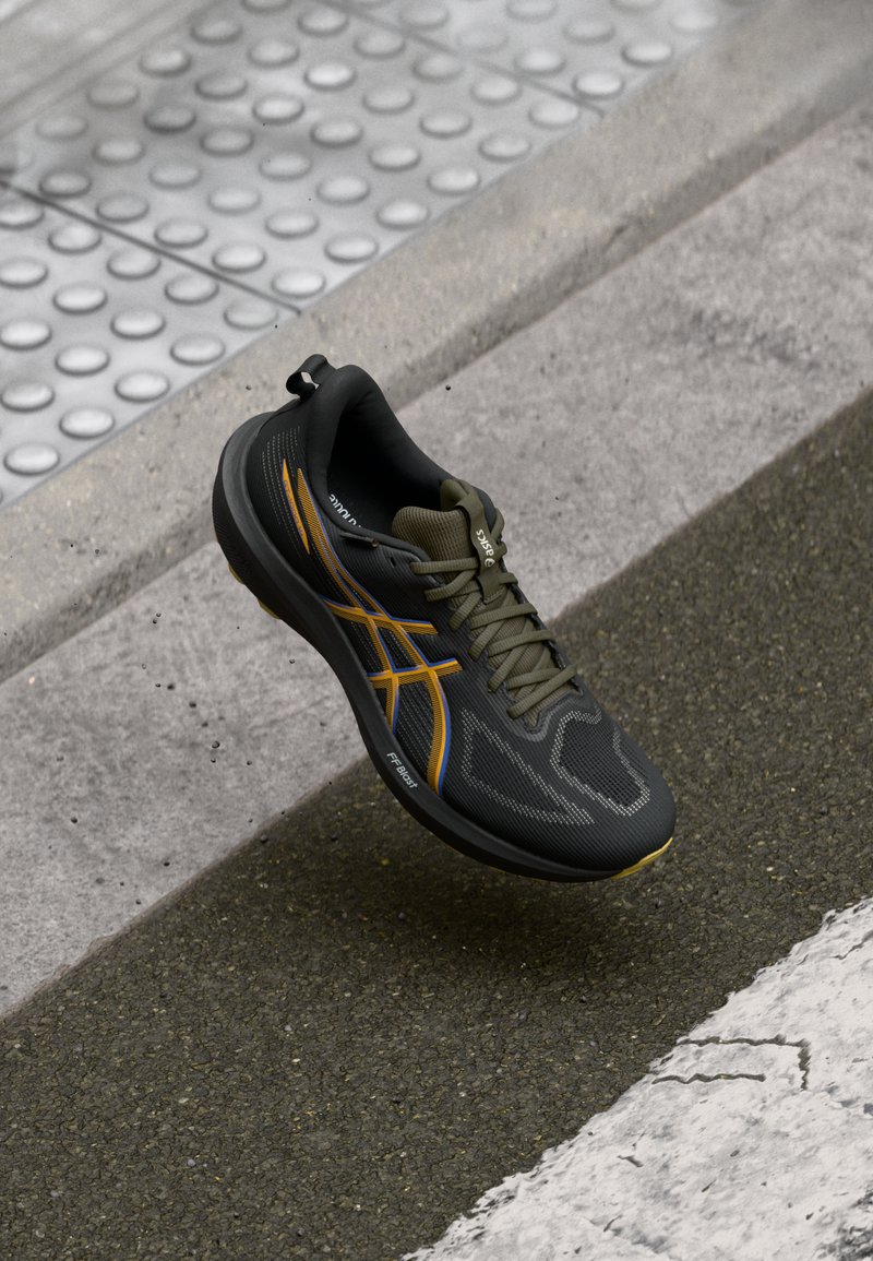 Black athletic shoe with a textured mesh upper, featuring orange and blue accents, a rounded toe, and a cushioned sole for support.
