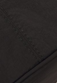 Černá látka s jemnou texturou má viditelné švy podél jednoho okraje. Design je jednoduchý a elegantní, ukazuje složený roh.