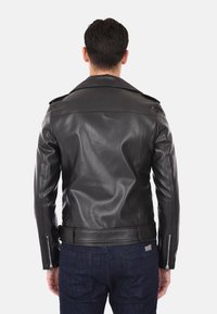 Giacca di pelle nera con design aderente, spalline sulle spalle e polsini con zip. Texture liscia con dettaglio in vita con cintura.