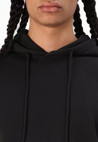 Felpa nera con cappuccio realizzata in un tessuto texturizzato. Presenta una tasca frontale, lacci per il cappuccio ed è progettata con una vestibilità rilassata.