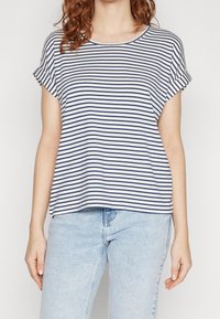 Pruhovaný top s krátkým rukávem v námořnické modré a bílé barvě, vyrobený z měkké tkaniny. Kulatý výstřih, volný střih a ohrnuté manžety. Nosený s světle modrými džíny.
