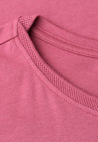 Primo piano della scollatura di una t-shirt rosa in cotone che mostra il colletto a costine e i dettagli delle cuciture.