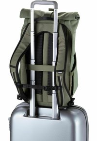 Sac à dos vert avec des sangles d'épaule réglables fixé sur la poignée extensible d'une valise rigide argentée. Matériau texturé, accents minimaux.