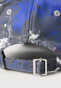 Zils un pelēks rakstains beisbola cepures mugura ar regulējamu auduma siksniņu un sudraba taisnstūra metāla sprādzi.