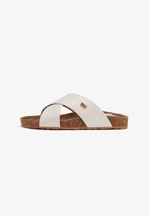 Sandale à bride croisée blanche avec une semelle en liège, fabriquée en cuir lisse et au design plat. Détails dorés remarquables sur la bride.
