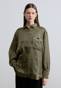 Melns krekls ar garām piedurknēm un pogām, ar zaļdzeltainu ģeometrisku rakstu, ar vienu krūšu kabatu un vaļēju piegriezumu.