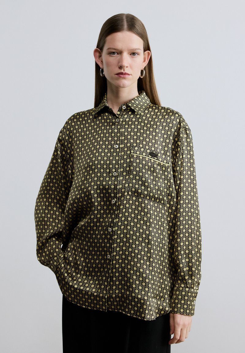 Cămașă cu nasturi, cu mâneci lungi, de culoare neagră, cu un model geometric verde-galben, având un buzunar la piept și croială lejeră.