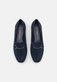 Mocasines de ante azul oscuro con un diseño plano, que presentan un adorno de cadena de metal en la parte frontal y detalles de costura alrededor de los bordes.