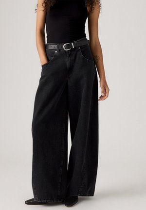 Jeans anchos negros de mezclilla con una cintura alta, con bolsillos frontales y un cinturón de cuero negro con una hebilla plateada.