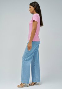 Camiseta ajustada rosa combinada con jeans de pierna ancha de un azul claro. La modelo lleva tacones de tiras. Tejido de algodón suave, diseño básico y un look relajado.