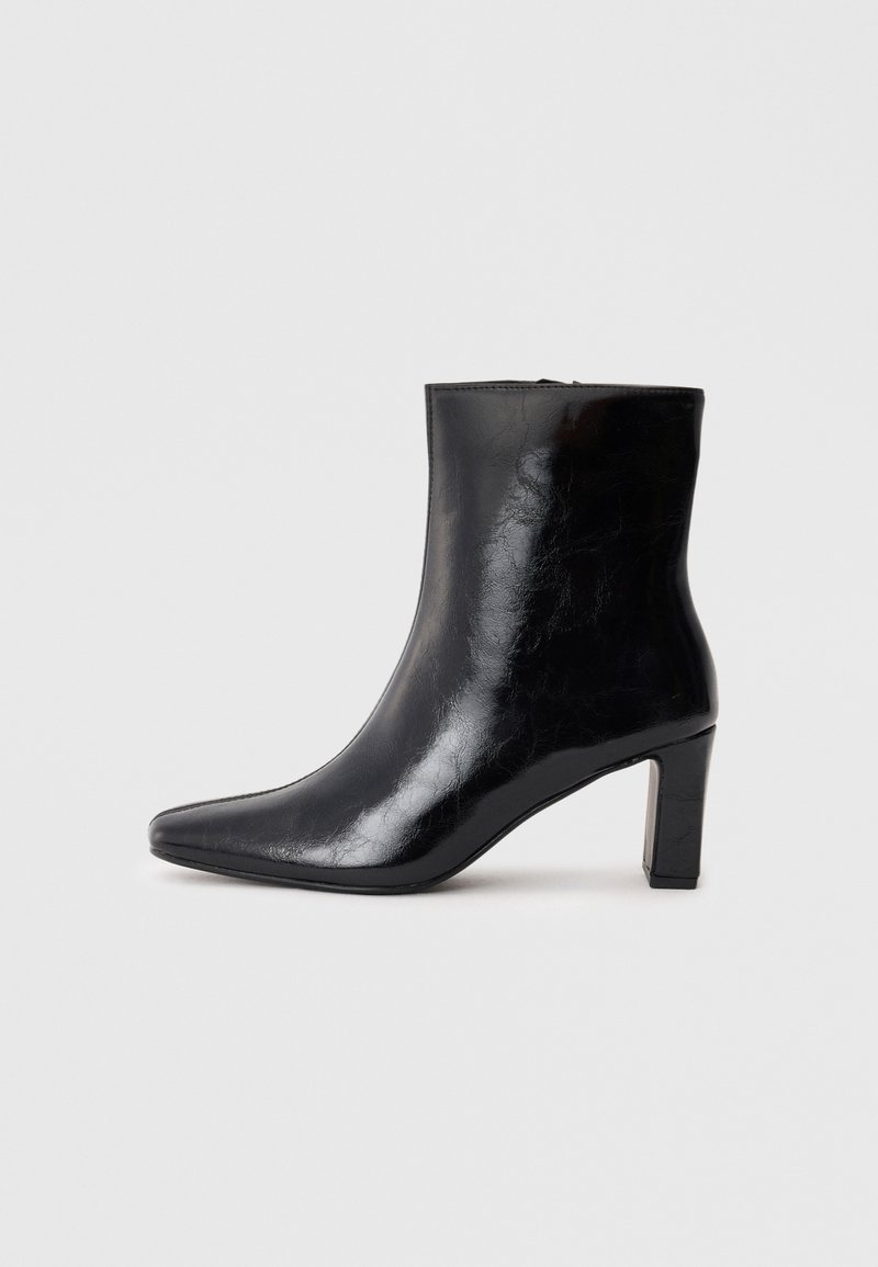 Schwarze Knöchelstiefel aus glänzendem Leder mit spitzem Zustand und mittelhohem Blockabsatz, mit glatter Textur und einfachem Design.
