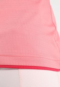 Top deportivo de color rosa claro, hecho de un tejido texturizado con un diseño ajustado y sutilezas de perforaciones, que presenta un dobladillo rojo en contraste.