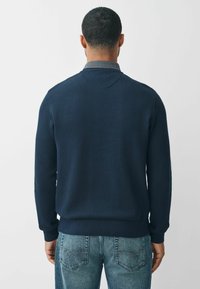 Granatowy sweter z prążkowanego dzianiny z kołnierzykiem, charakteryzujący się teksturowanym wykończeniem i prostym dołem, zestawiony z jasnoniebieskimi dżinsami.