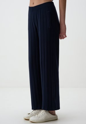 Pantalons larges bleu marine en tissu doux avec des côtes verticales, dotés d'une poche sur le côté et portés avec des baskets blanches.