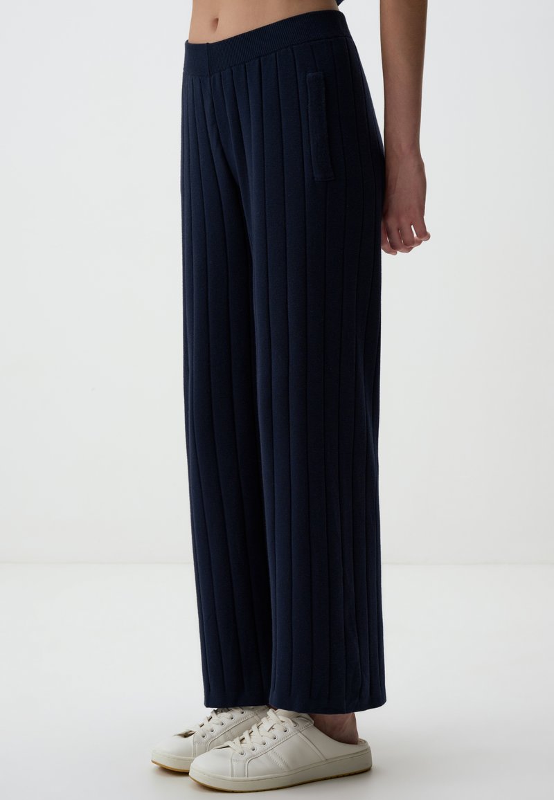 Marine wijde pijpenbroek van zachte stof met verticale ribbels, voorzien van een zijzak en gecombineerd met witte sneakers.