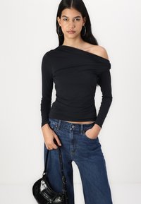 Haut noir à épaules dénudées avec des détails froncés, associé à un jean bleu taille haute et un petit sac à main noir.