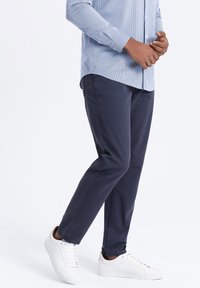 Chinos navy en tissu mélangé coton avec une texture lisse, coupe slim et associés à des baskets blanches. La chemise présente des rayures bleu clair.