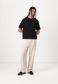 Svart bomull t-skjorte med korte ermer, kombinert med lyse beige avslappede bukser. Modellen har på seg svarte sneakers med brune såler. Enkel design.
