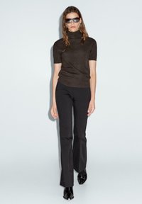 Brun kortärmad polo tröja med en åtsittande design, ihop med svarta utsvängda byxor. Modellen bär solglasögon och enkla örhängen.