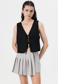 Svart kort topp med djup V-urtavla och dragsnörning, ihop med en ljusgrå plisserad mini-kjol. Slät tygkvalitet och figurnära design.