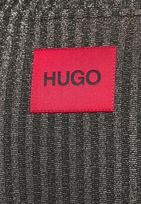Tessuto intrecciato nero e argento con strisce verticali; presenta un'etichetta rossa ben visibile con la scritta "HUGO" in testo nero.