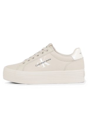 Baskets compensées beige Calvin Klein avec un laçage à l'avant, logo sur le côté et col rembourré sur fond blanc.