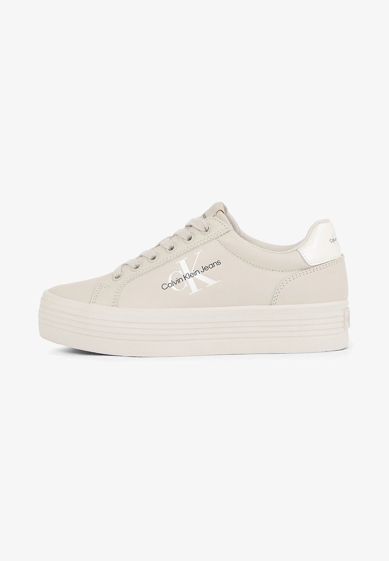 Baskets compensées beige Calvin Klein avec un laçage à l'avant, logo sur le côté et col rembourré sur fond blanc.