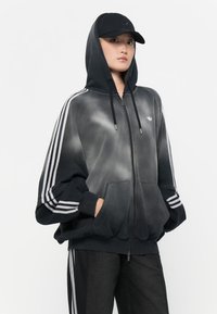 Black and gray gradient hoodie with white stripes on sleeves, front zip, kangaroo pockets, and a drawstring hood. Worn with black pants.