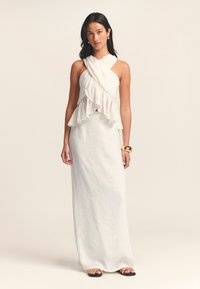 Robe maxi blanche avec un corsage asymétrique à volants et une silhouette ajustée. Fabriquée en tissu léger, elle présente une texture lisse.