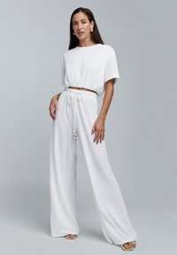 Witte geribbelde cropped top gecombineerd met witte wijde broek. De broek heeft een tailleband met trekkoord en decoratieve kralen. Soepele stofstructuur.