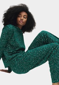 Grøn, mønstret to-delt sæt bestående af en løstsiddende top og brede bukser med en tekstureret, pletlignende design i sort og hvide accenter.