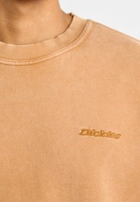Felpa color cognac con collo a girocostina. Il tessuto ha una trama morbida con un logo "Dickies" ricamato in oro sul petto.