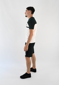 Camiseta de manga corta en bloque de color con secciones en verde oscuro y blanco, combinada con pantalones cortos verdes oscuros. Zapatillas deportivas negras completan el look.