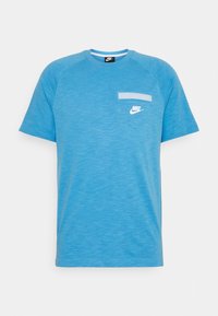 Camiseta Nike de color azul claro, fabricada en un tejido suave, que presenta mangas cortas, cuello redondo y un pequeño bolsillo en el pecho con un logo blanco.