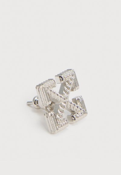 Pendiente de botón tono plateado con forma de cuatro flechas que apuntan hacia afuera desde el centro, con detalles texturizados y acanalados.