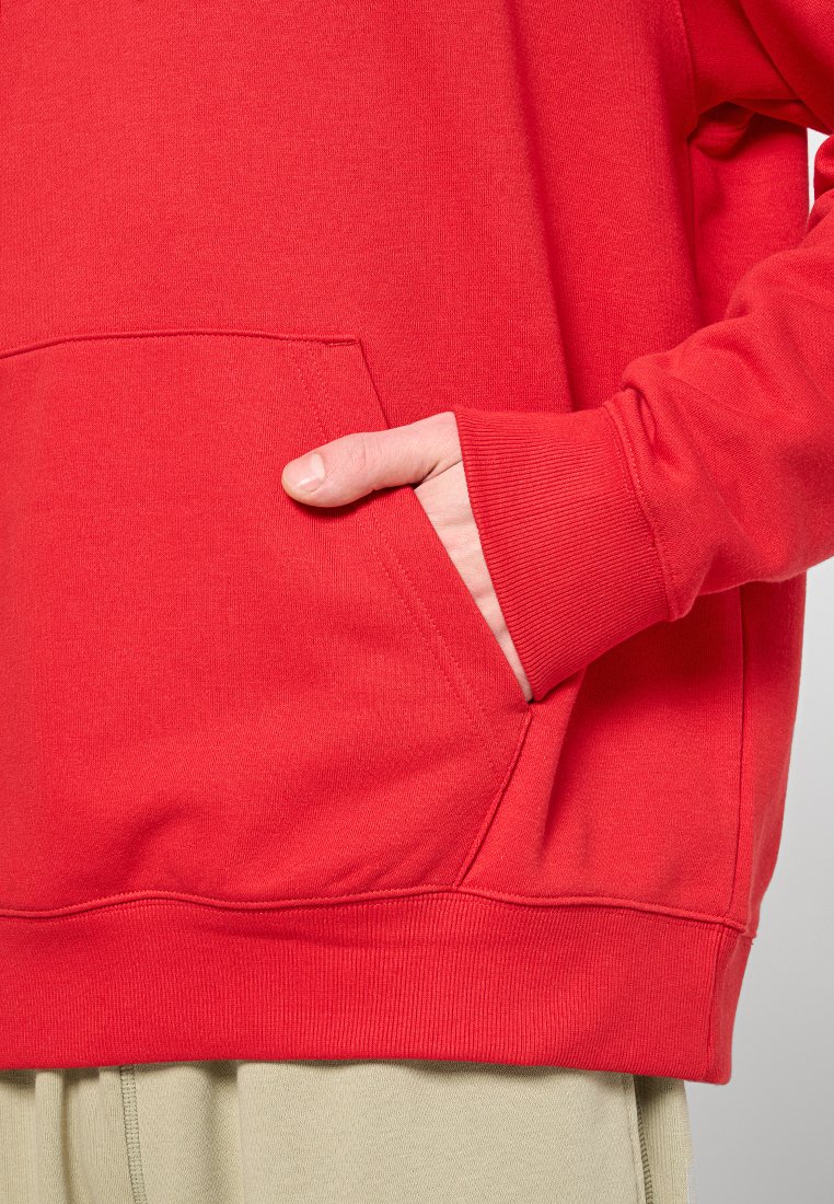 Sweat à capuche rouge avec une poche avant, des poignets côtelés et une texture douce. Le design est décontracté, avec une coupe ample.