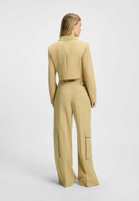 Geknipte beige blazer met een getailleerde pasvorm, voorzien van een reverskraag. Gecombineerd met beige wijde broek met twee cargopockets.